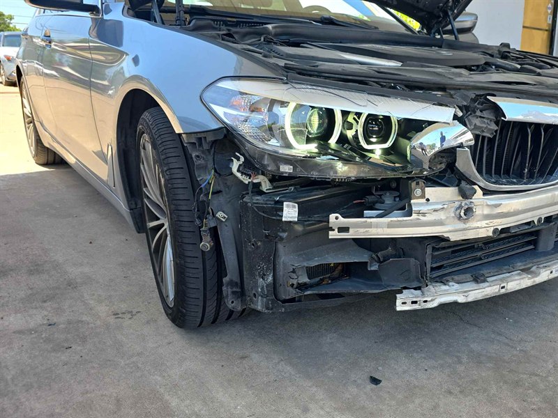 Un BMW Serie 5 gris antes de la reparación, con la defensa delantera arrancada y el área del faro dañada