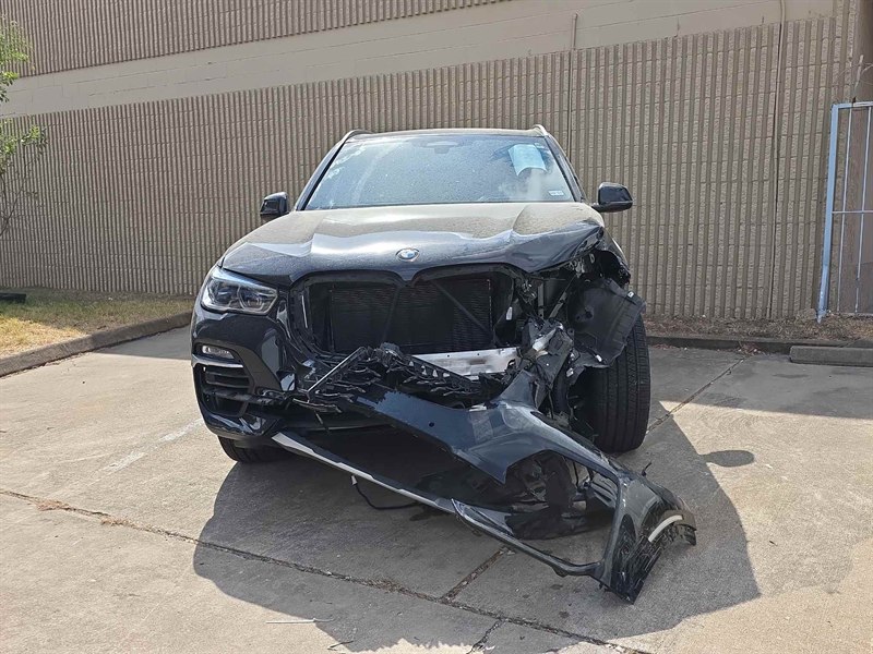 Una BMW X5 negra antes de la reparación, con la defensa delantera arrancada y la parrilla y la salpicadera aplastadas