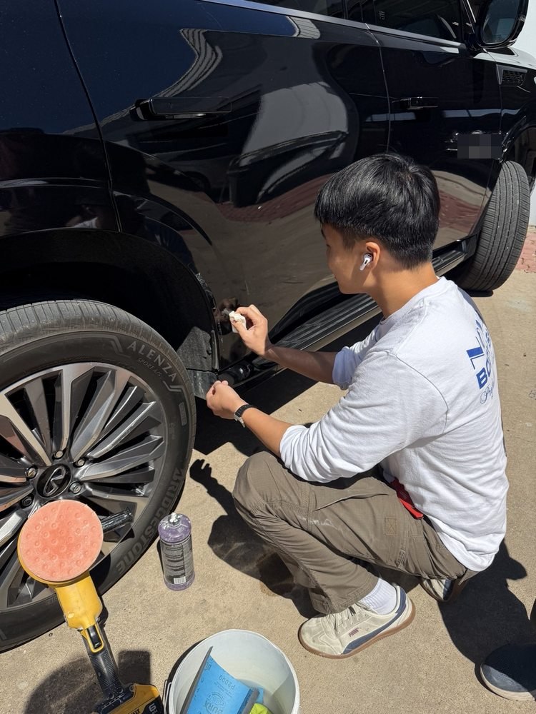 A Nova Body Shop technician doing careful touch-up work by hand on a black SUV